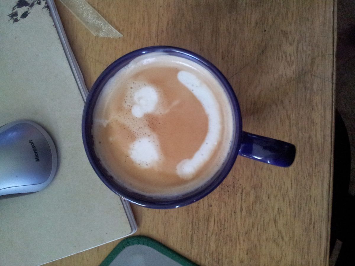 Navy mug of coffee seen from above, with a white crescent of milk on a desk