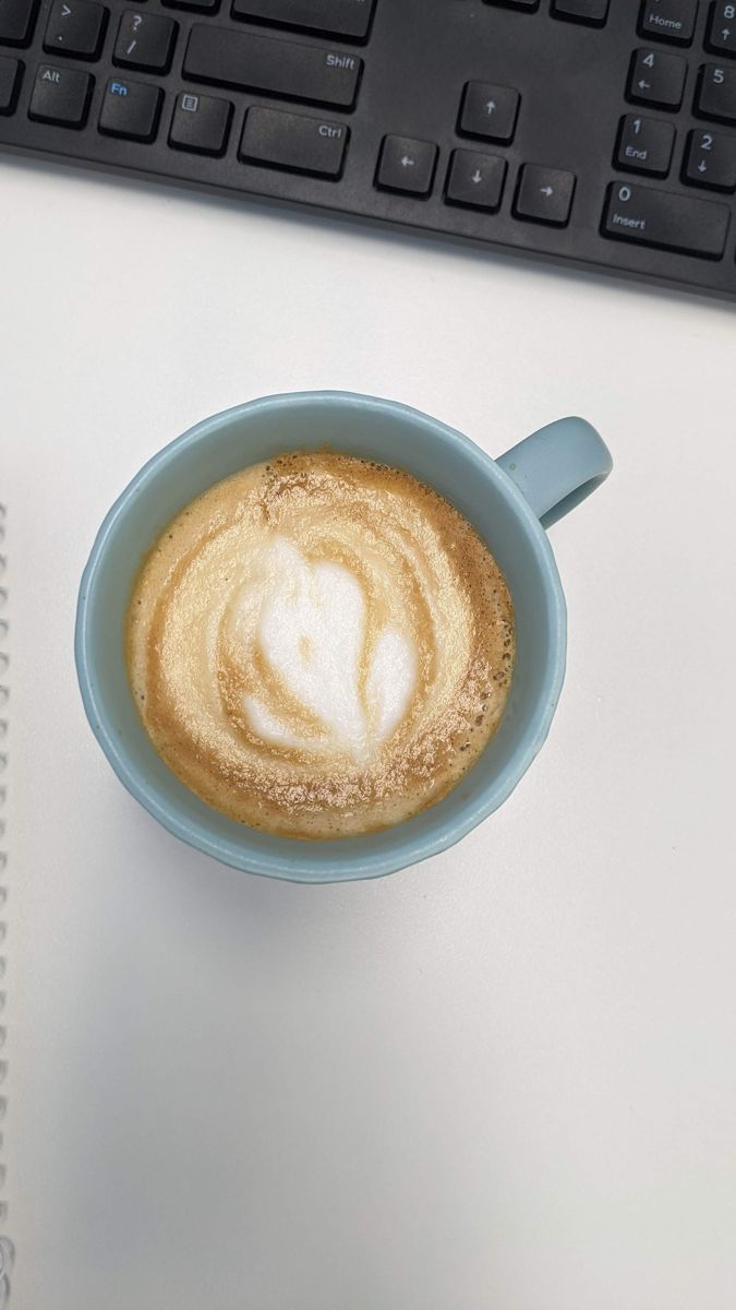 Pale blue mug next to a keyboard, with a lopsided heart in the foam