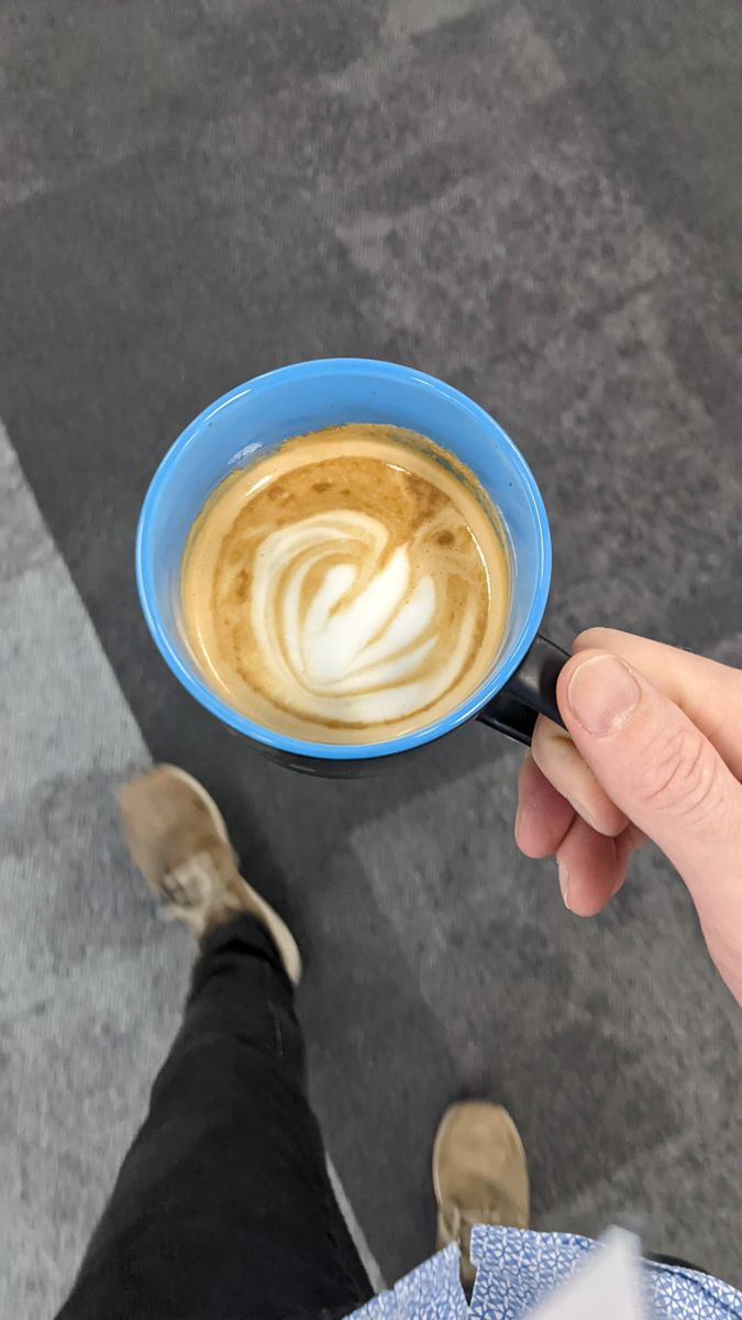 Blue mug held over a carpet, with a swirling white fern in the coffee