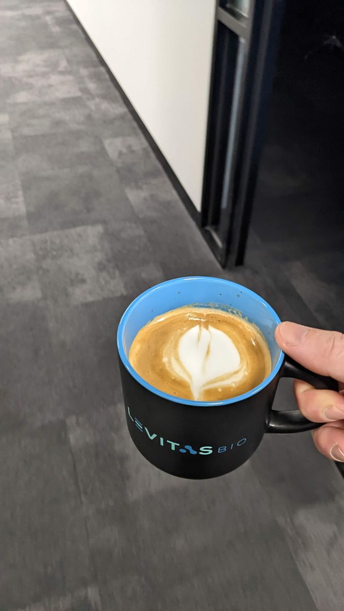 Blue mug held in one hand, with a small white leaf shape in the foam