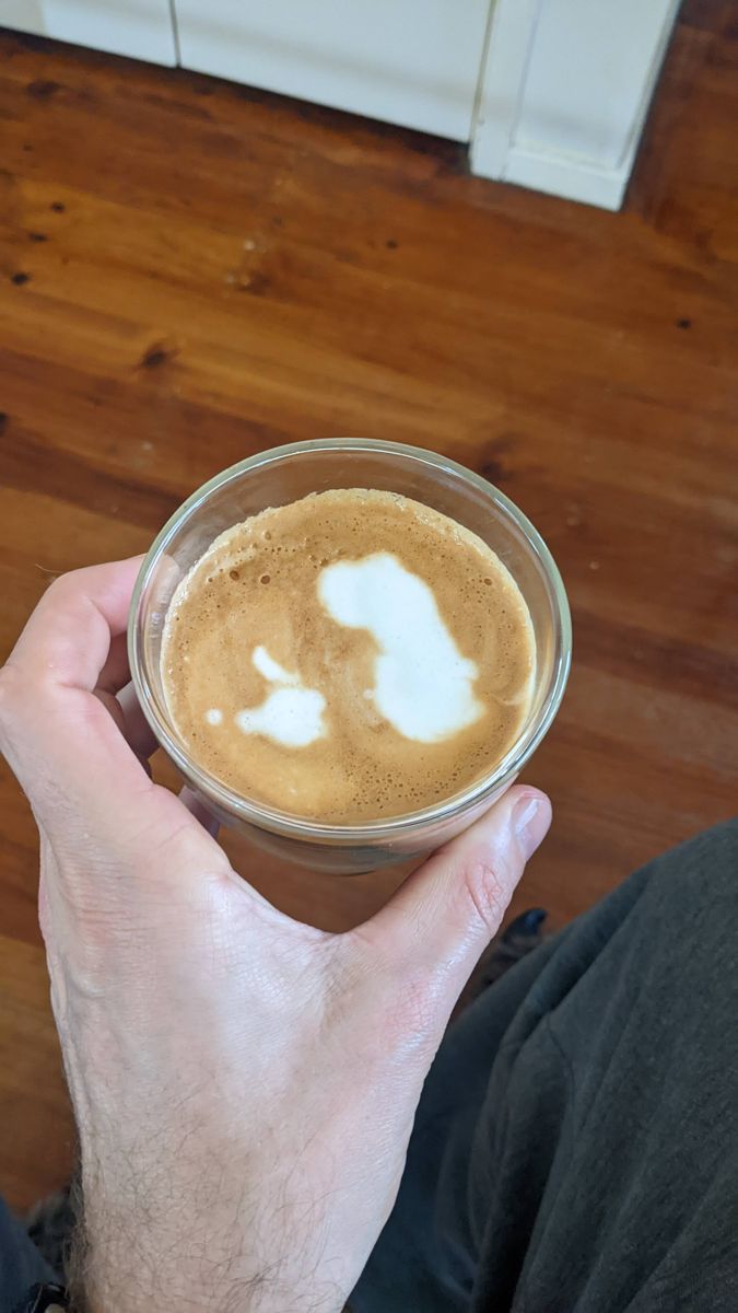Hand holding a glass of coffee with irregular white blobs of milk on top