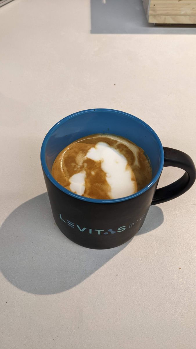 Black mug on a light floor, with a large white ghost-like shape in the coffee